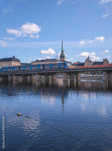 Photography Blue commuter train on a bridge passing the old town Gamla Stan and the church t