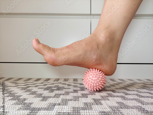 Woman using a pink spiky massage ball on a rug to relieve pain in the arch of her foot photo