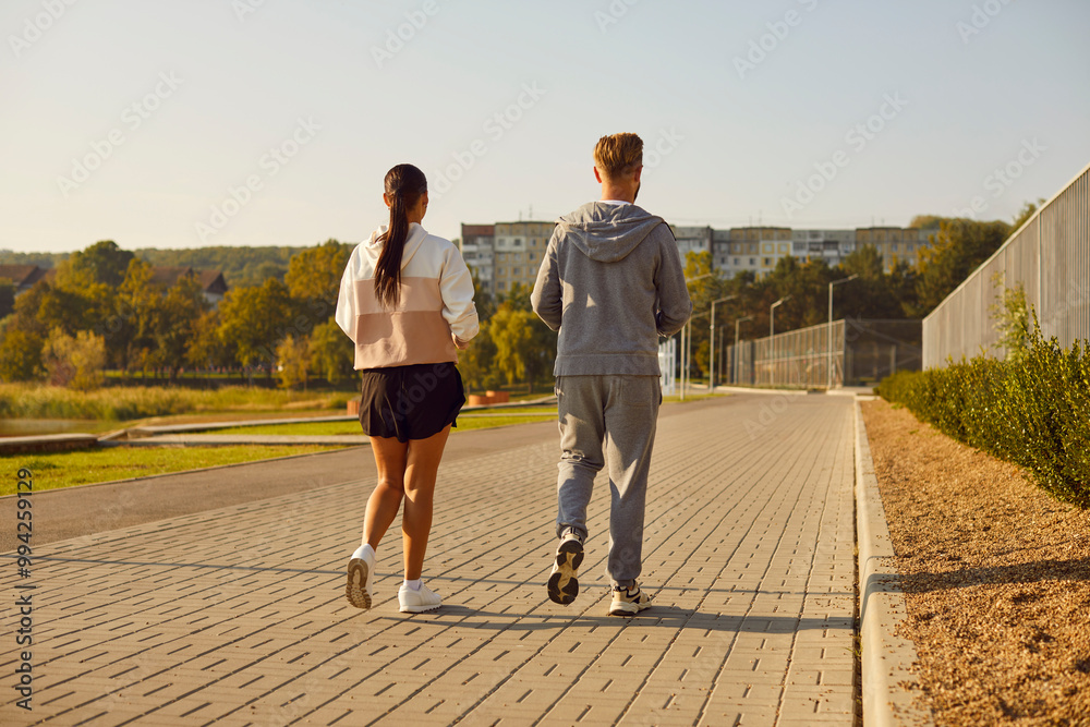 Fototapeta premium Back view of sporty young man and woman wearing sportswear jogging in the park having sport workout for health in nature. Couple running in nature. Jog exercising and healthy lifestyle concept.