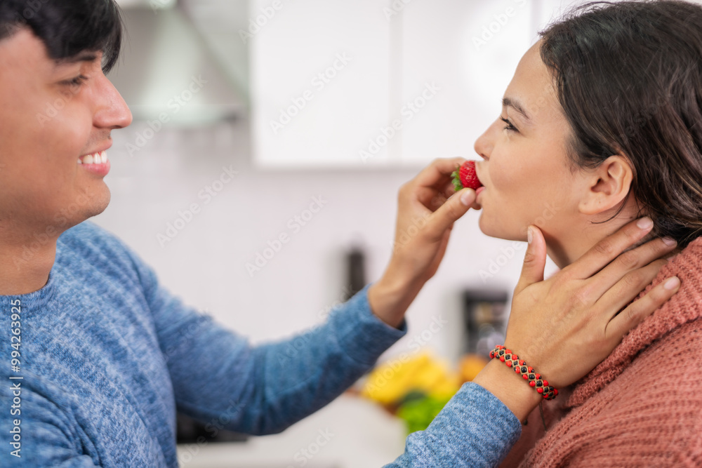 Hispanic man feeding strawberry to woman in kitchen Hispanic man feeding strawberry to woman in kitchen