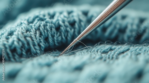 In this image, a close-up of a needle threading through blue knitted fabric is presented, highlighting the intricacy and skillfulness involved in the knitting craft.