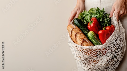 A string netted bag contains fresh produce such as red bell peppers, cucumber, fresh greens, and a loaf of bread, highlighting a sustainable shopping choice. photo