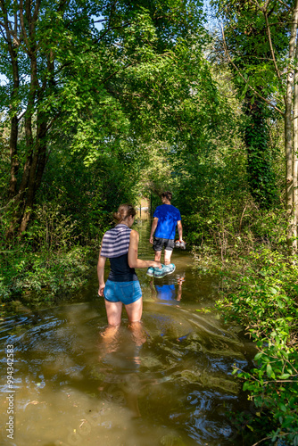 Young People Walk On Flooded Hiking Path Through Forest At High Water In Danube Wetlands National Park In Austria