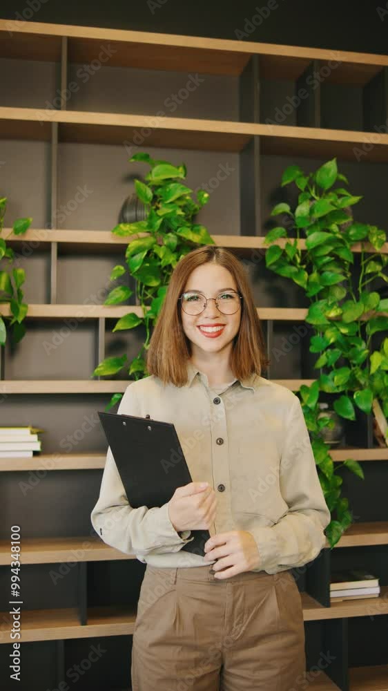 A Professional Young Woman Wearing Stylish Glasses is Holding a Clipboard while Seated in a Modern Office Setting that Exudes Inspiration,vertical video A Professional Young Woman Wearing Stylish Glasses is Holding a Clipboard while Seated in a Modern Office Setting that Exudes Inspiration,vertical video