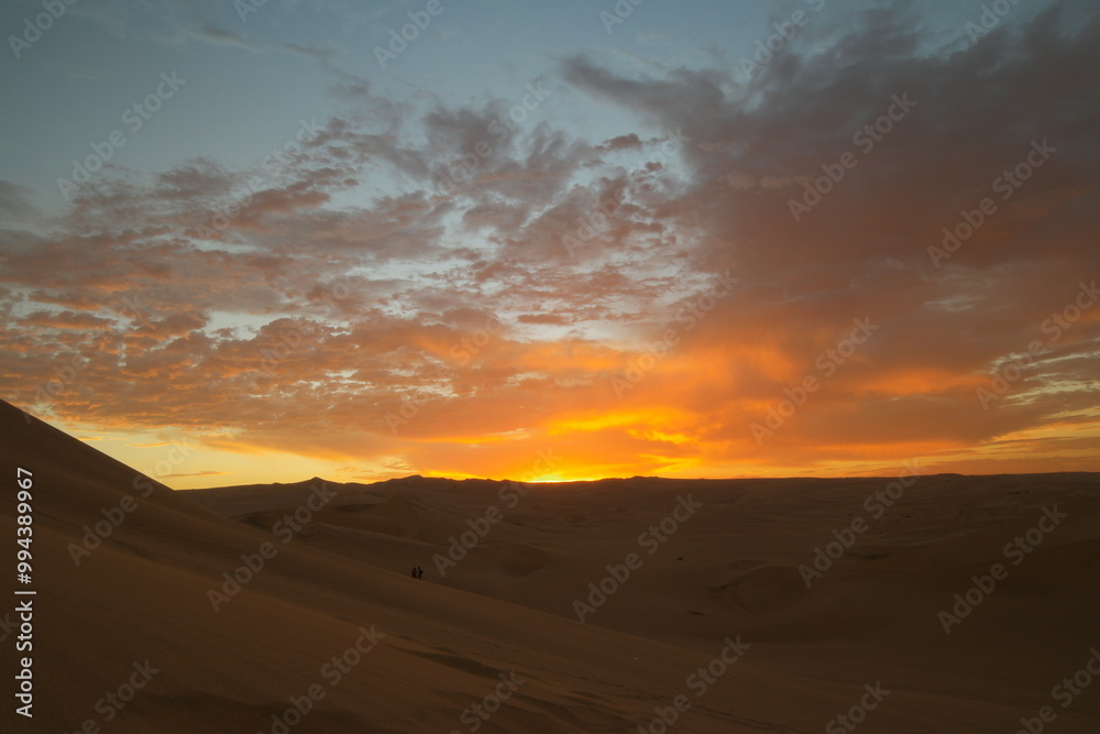 Obraz premium Stunning sunset over the Huacachina desert in Peru, illuminating the sky with vibrant colors after a day of exploration and adventure