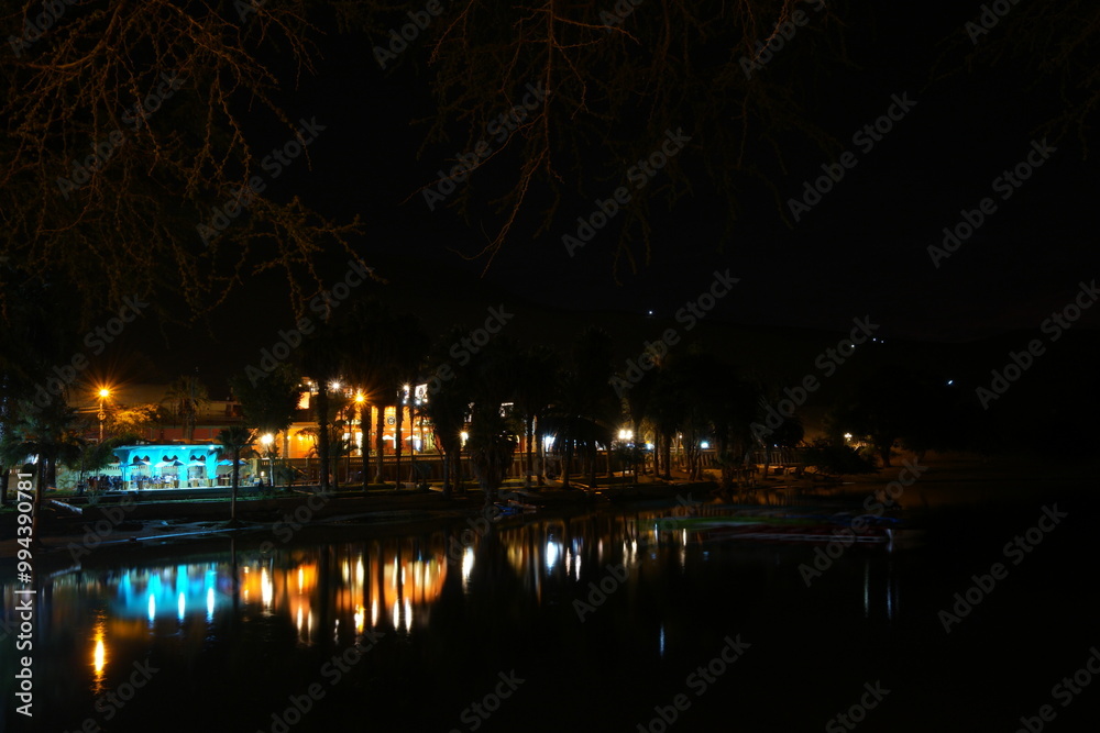Night view of Huacachina Oasis in Peru with illuminated buildings reflecting on calm water Night view of Huacachina Oasis in Peru with illuminated buildings reflecting on calm water