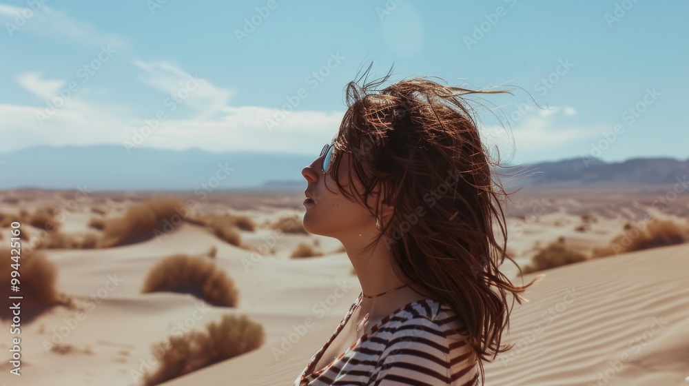 Obraz premium A serene woman with flowing hair stands in a sunlit desert, peacefully connecting with nature.
