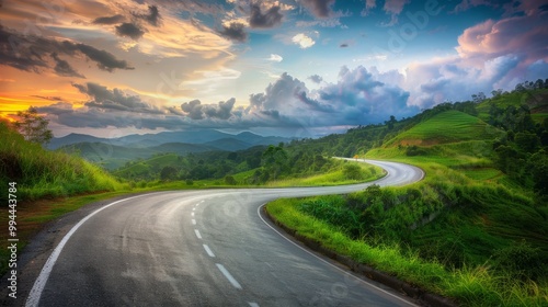 A mesmerizing curvy road cutting through rolling green hills, kissed by a vibrant sunset.