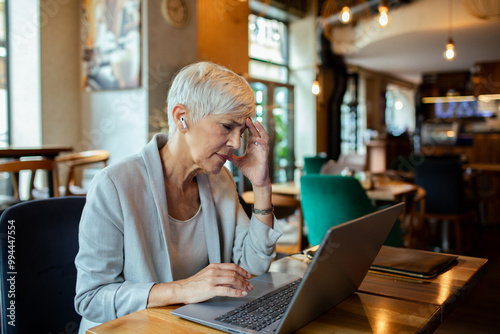 Senior businesswoman working on laptop in a cafe with wireless earbuds photo