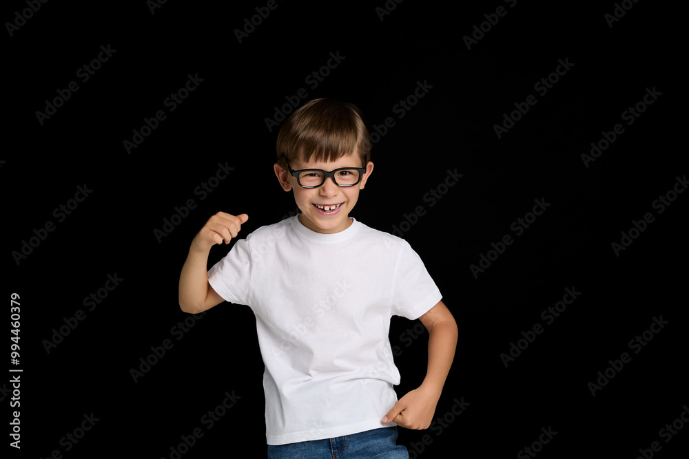 Fototapeta premium Smiling schoolboy in eyeglasses, wearing white t-shirt, isolated black background.