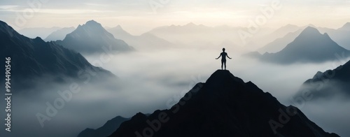 Person standing triumphantly on a mountain peak overlooking misty valleys at ...