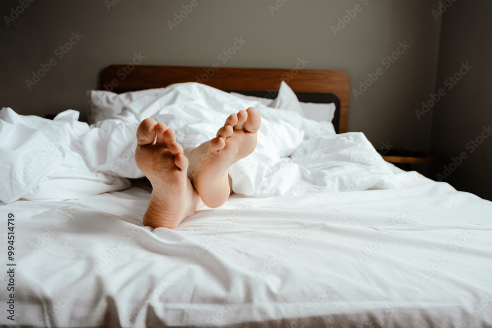 Bare Feet Peeking From Under Cozy White Sheets On Bed Bare Feet Peeking From Under Cozy White Sheets On Bed
