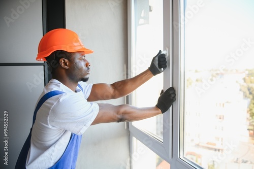 Young African Repairman In Overalls Installing Window