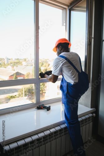 Young African Repairman In Overalls Installing Window