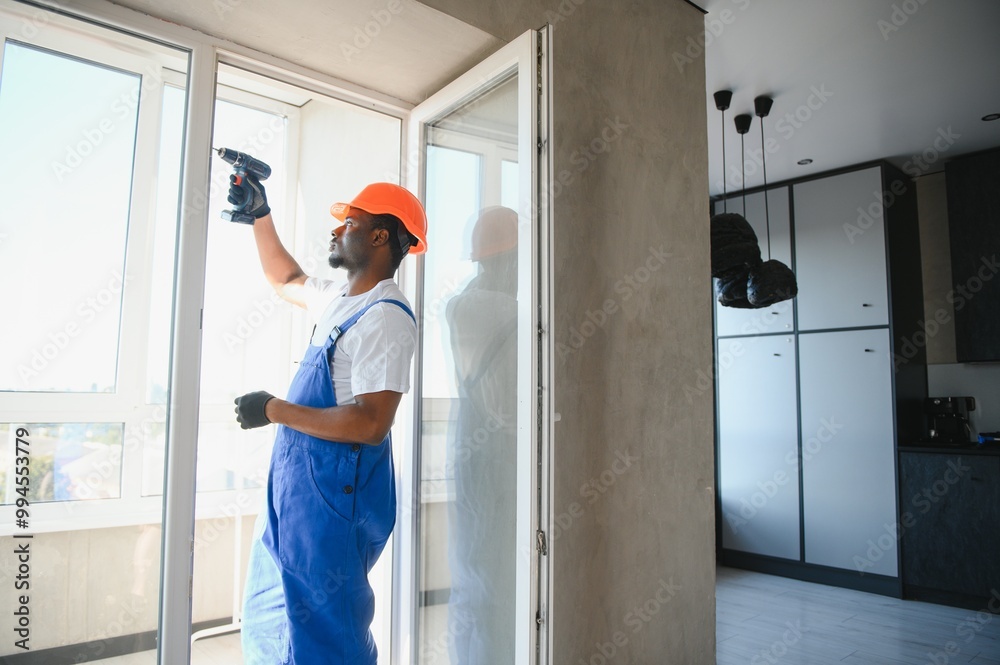 Workman in overalls installing or adjusting plastic windows in the living room at home Workman in overalls installing or adjusting plastic windows in the living room at home