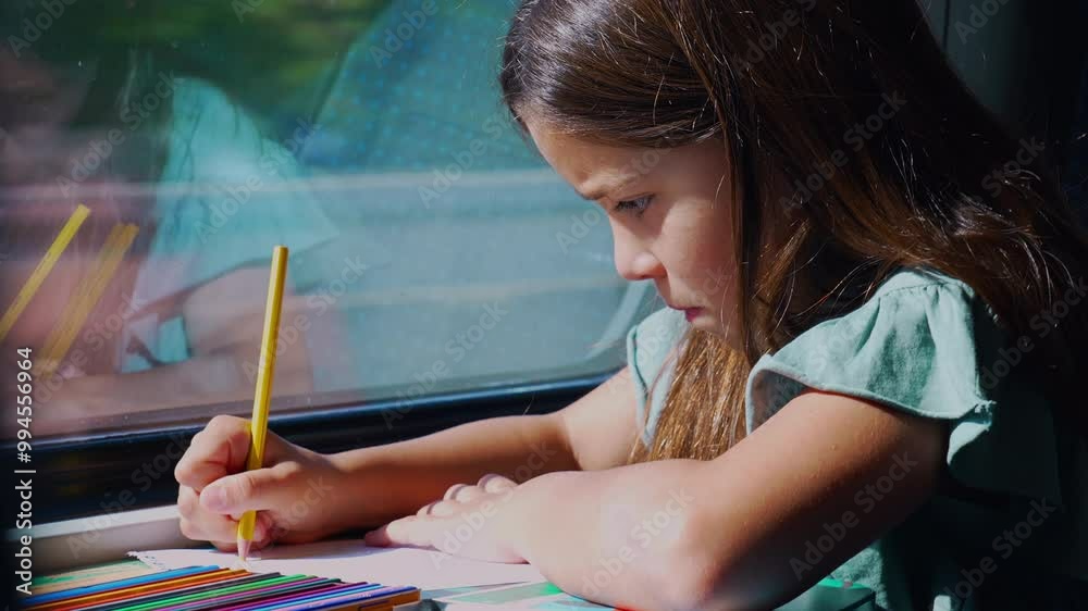 Young girl deeply focused on drawing with a pencil while traveling on a train, her reflection showing on the window as she concentrates on her artwork