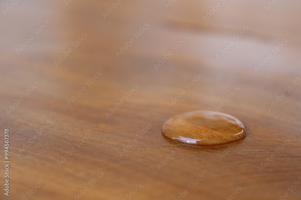 Drop of water reflecting light on a waterproof wooden surface with a beautiful caramel brown texture. Drop of water reflecting light on a waterproof wooden surface with a beautiful caramel brown texture.