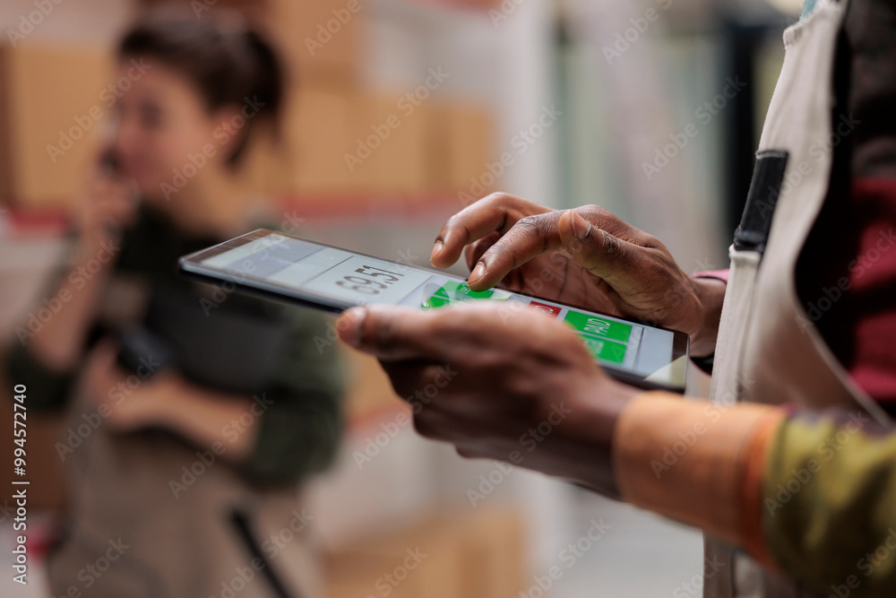 African american worker checking postal form on tablet computer, searching clients parcel before start preparing order. Storehouse employee supervising cardboard boxes in storage room. Close up African american worker checking postal form on tablet computer, searching clients parcel before start preparing order. Storehouse employee supervising cardboard boxes in storage room. Close up