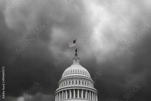 A black and white photo of the United States Capitol building with a flag on top. The sky is cloudy and the building is surrounded by a white fence