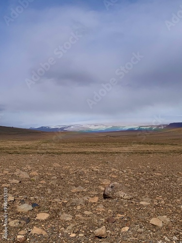 Breathtaking rocky surfaced landscape. Mountain range covered in snow appears in distance. Rainbow paints the light into colors. Atmosphere of remotenes, harsh, yet beautiful natural scenery. photo