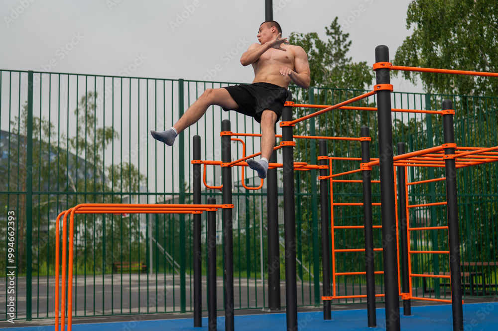 Fototapeta premium A shirtless man is doing a workout on the horizontal bars outdoors.