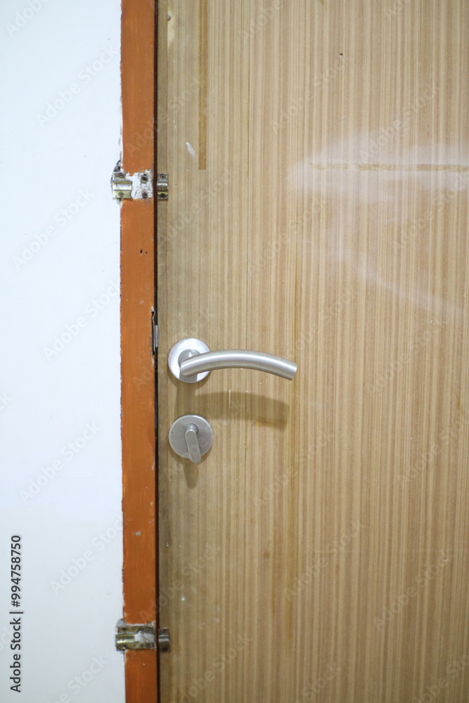 A close-up of a wooden door with a silver handle, slightly ajar, revealing a white wall and an orange frame. A close-up of a wooden door with a silver handle, slightly ajar, revealing a white wall and an orange frame.