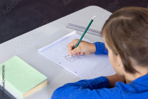 Writing math equations in notebook, boy focusing on schoolwork at desk