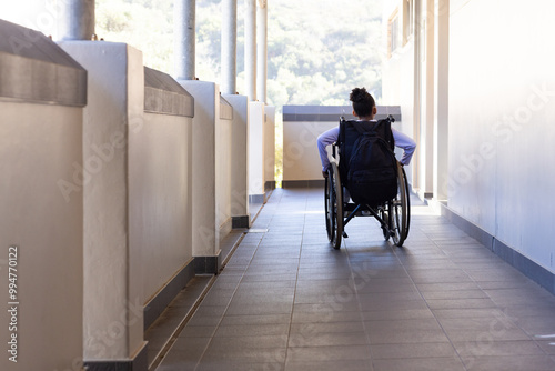 In school, student in wheelchair moving through hallway, carrying backpack