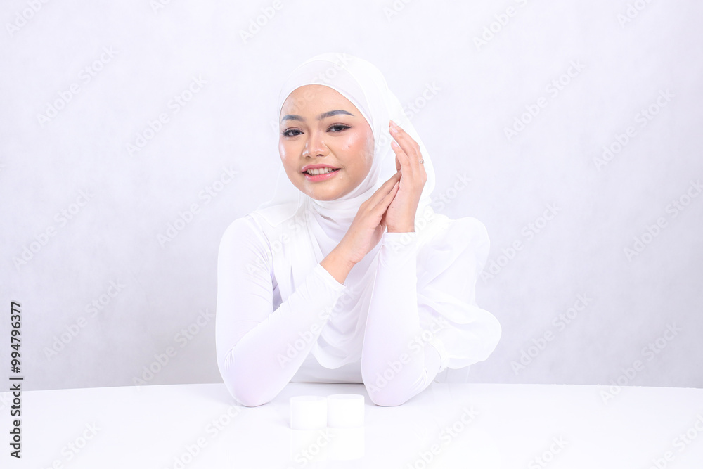 Beautiful young hijab woman face view big smile look at camera center aligned behind cosmetic cream bottle isolated white background. concept Cosmetology, beauty, spa, Face care, Facial treatment Beautiful young hijab woman face view big smile look at camera center aligned behind cosmetic cream bottle isolated white background. concept Cosmetology, beauty, spa, Face care, Facial treatment