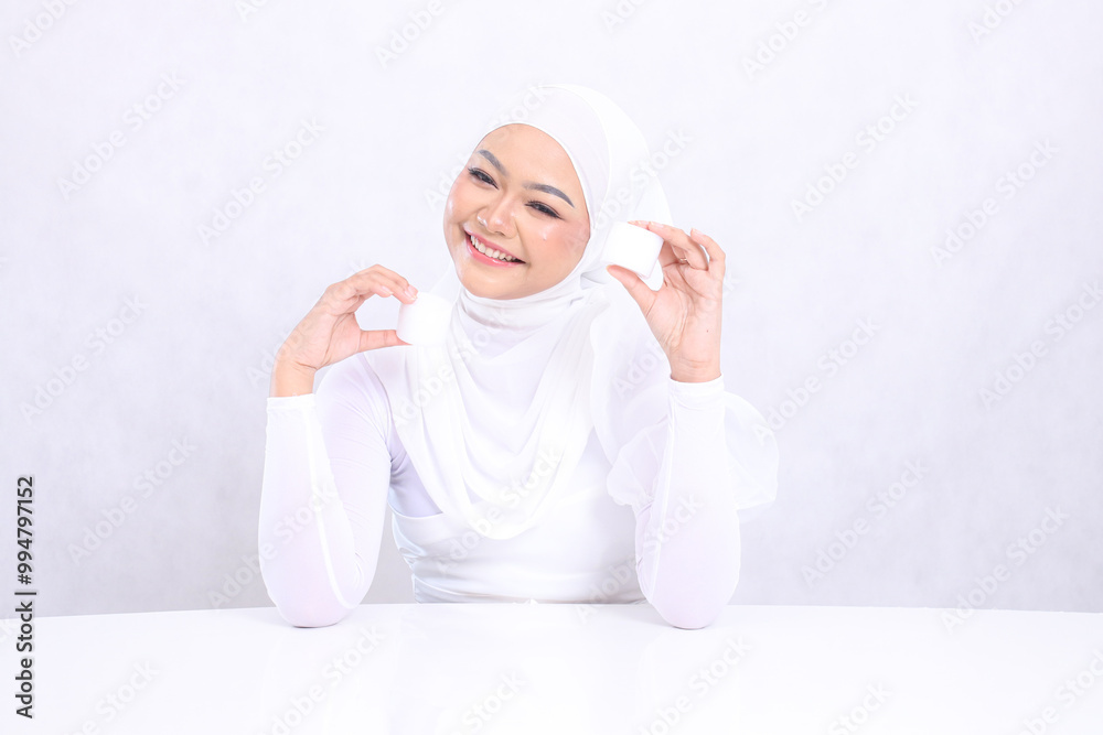 Beauty Beautiful young hijab woman laughing sideways to the camera both hands holding cosmetic cream satisfied in her facial care routine on white background. Facial treatment, Natural makeup Beauty Beautiful young hijab woman laughing sideways to the camera both hands holding cosmetic cream satisfied in her facial care routine on white background. Facial treatment, Natural makeup