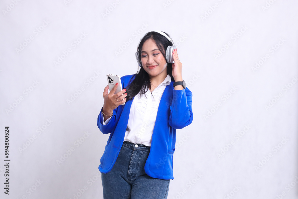 beautiful mature office woman wearing blue formal suit standing candid smile while carrying smartphone and using headphone. for technology, lifestyle, music, entertainment content beautiful mature office woman wearing blue formal suit standing candid smile while carrying smartphone and using headphone. for technology, lifestyle, music, entertainment content