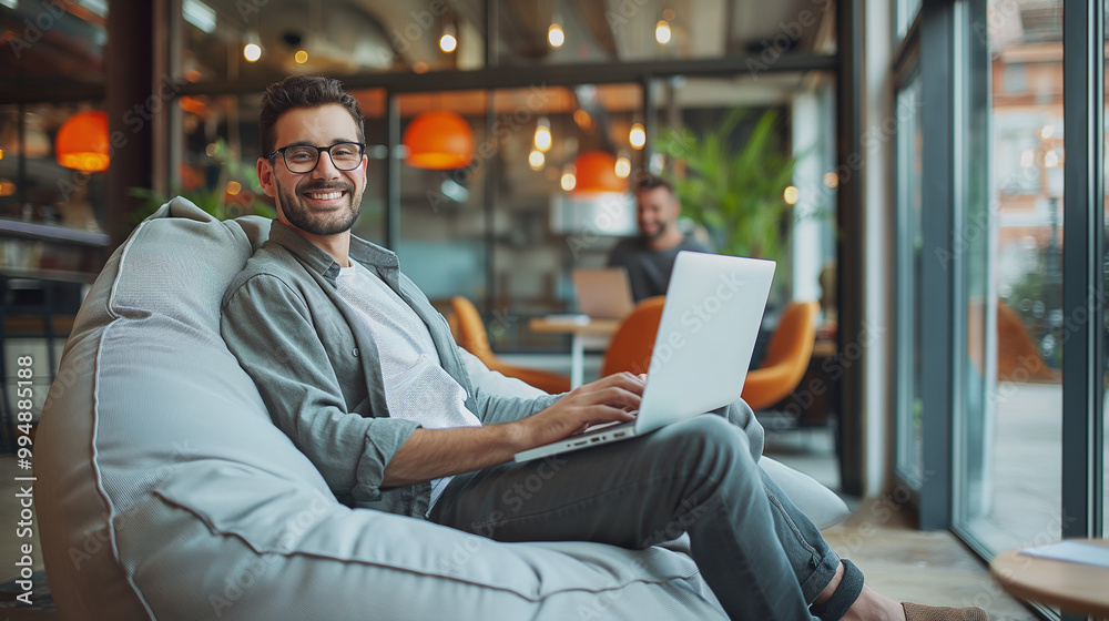 happy young businessman sitting in bag chair in modern office working on laptop happy young businessman sitting in bag chair in modern office working on laptop