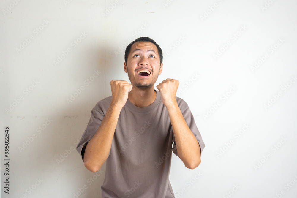 Overjoyed Asian young men in white isolated white background celebrating success with clenched fists Overjoyed Asian young men in white isolated white background celebrating success with clenched fists
