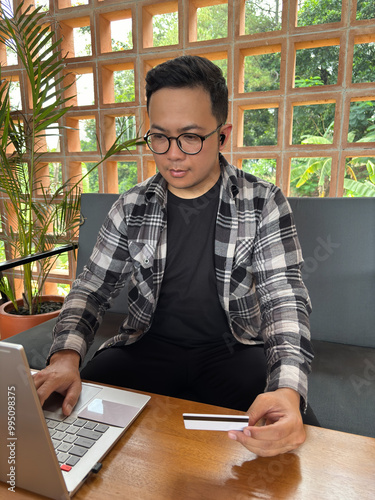 A man typing on a laptop while holding a credit card