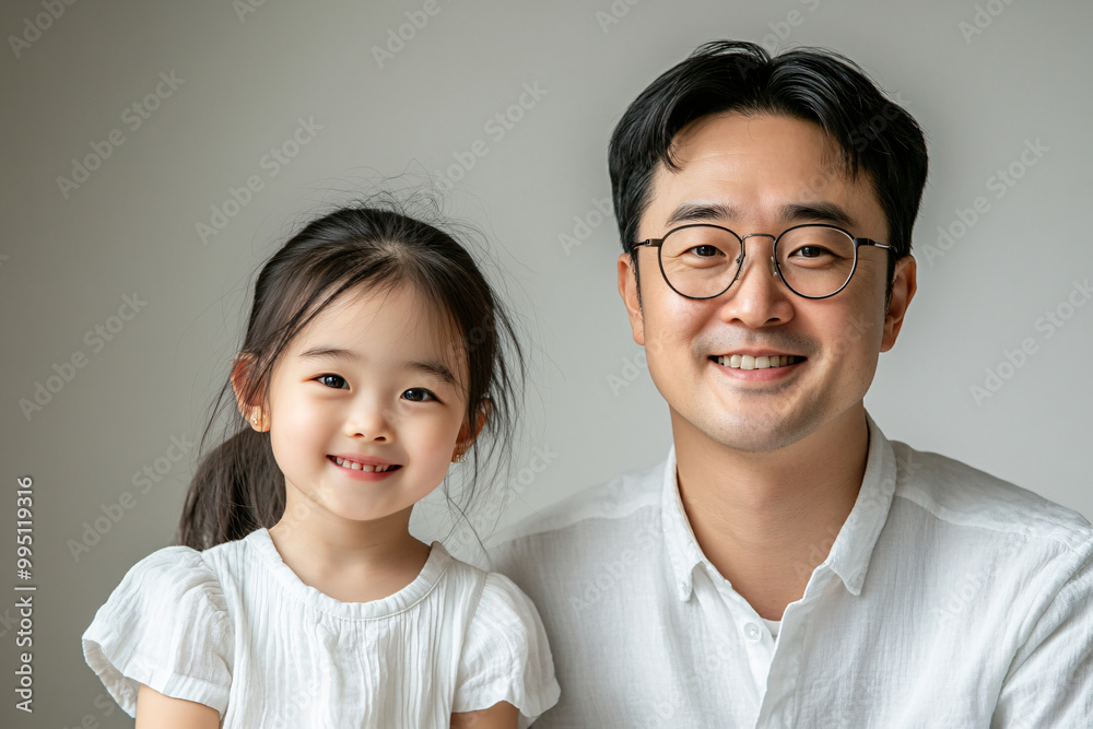 Young Chinese father and cute daughter interacting and smiling in plain background, dressed in simple Uniqlo clothes, family photo portrait.