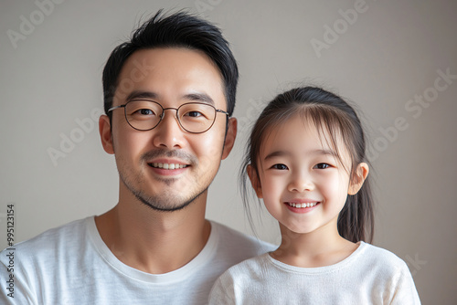 Young Chinese father and cute daughter interacting and smiling in plain background, dressed in simple Uniqlo clothes, family photo portrait. photo