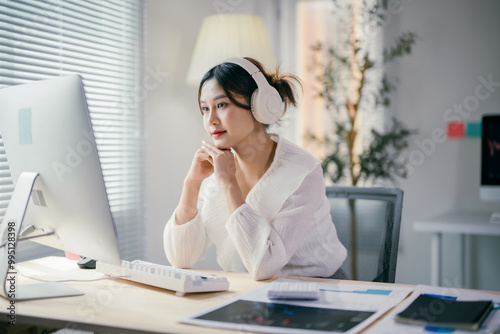Focused businesswoman wearing headphones working at her desk in the office listening to music or participating in a virtual meeting