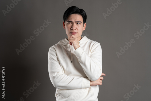 Portrait of Asian man wearing hoodie and posing on gray background.