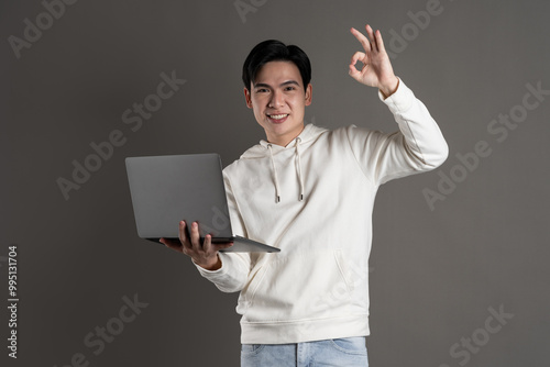 Portrait of Asian man wearing hoodie and posing on gray background.