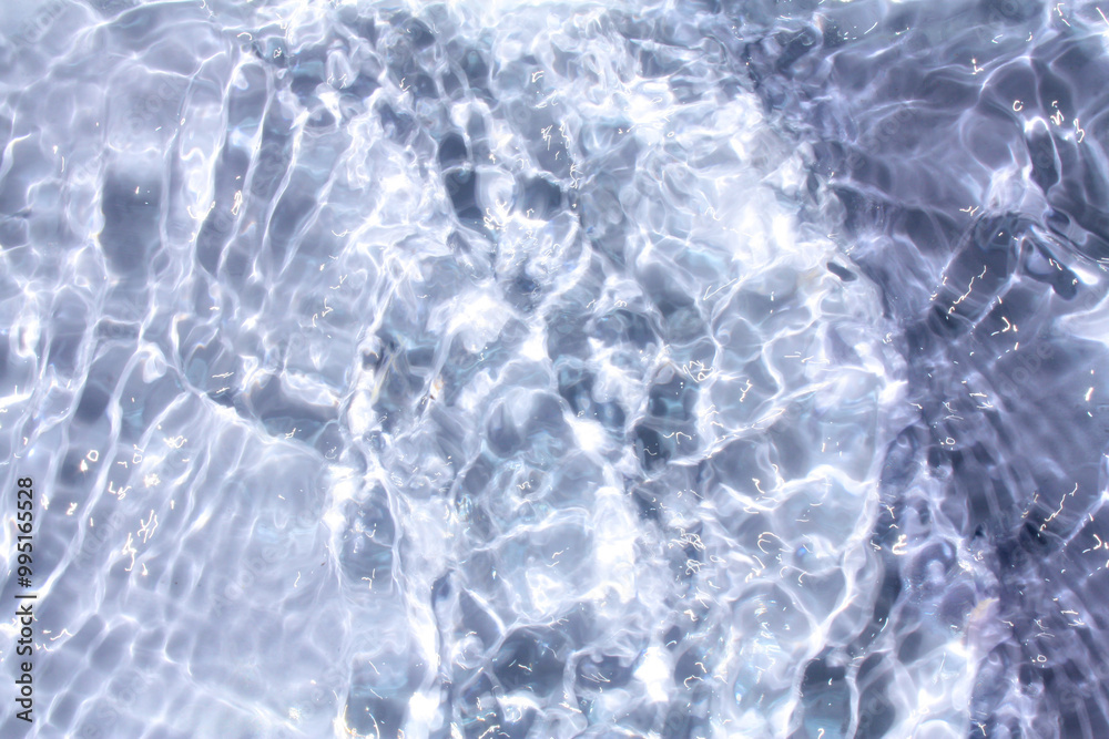 Bluewater waves on the surface ripples blurred. Defocus blurred transparent blue colored clear calm water surface texture with splash and bubbles. Water waves with shining pattern texture background.
