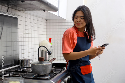 Young Asian woman using smartphone in kitchen while cooking