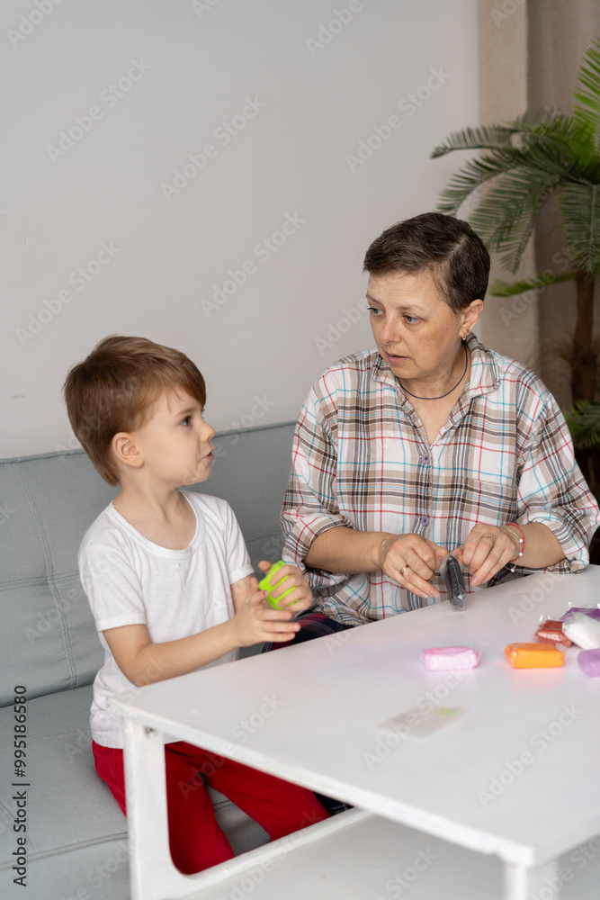 Middle aged mother and her small son sculpting with play dough or plasticine at table in the living room at home. family, creativity and craft Middle aged mother and her small son sculpting with play dough or plasticine at table in the living room at home. family, creativity and craft