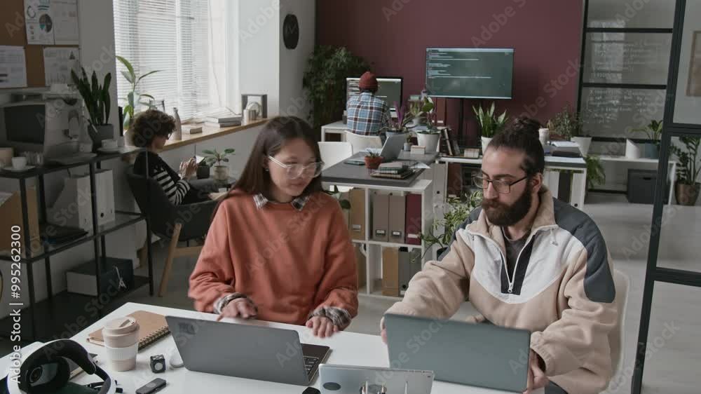 Medium timelapse shot of young biracial female software developer working on project at IT startup, writing computer code, the collaborating with Middle Eastern colleague, discussing problems