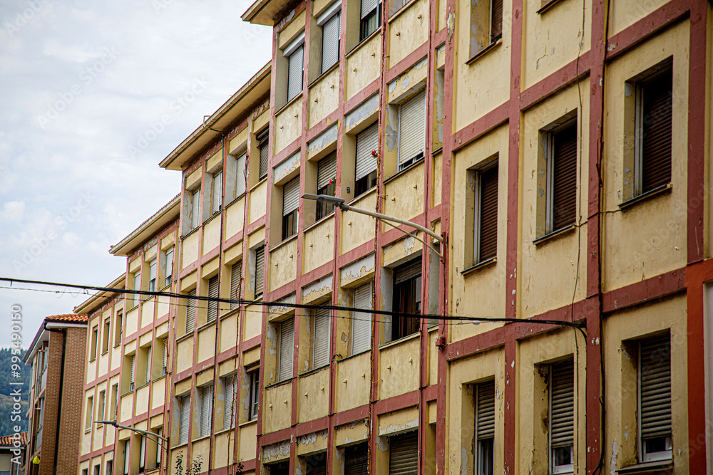 The image features a multi-story residential building with a classic, rustic look, combining brick and white concrete walls. It reflects a typical urban or suburban setting, with evenly spaced windows The image features a multi-story residential building with a classic, rustic look, combining brick and white concrete walls. It reflects a typical urban or suburban setting, with evenly spaced windows