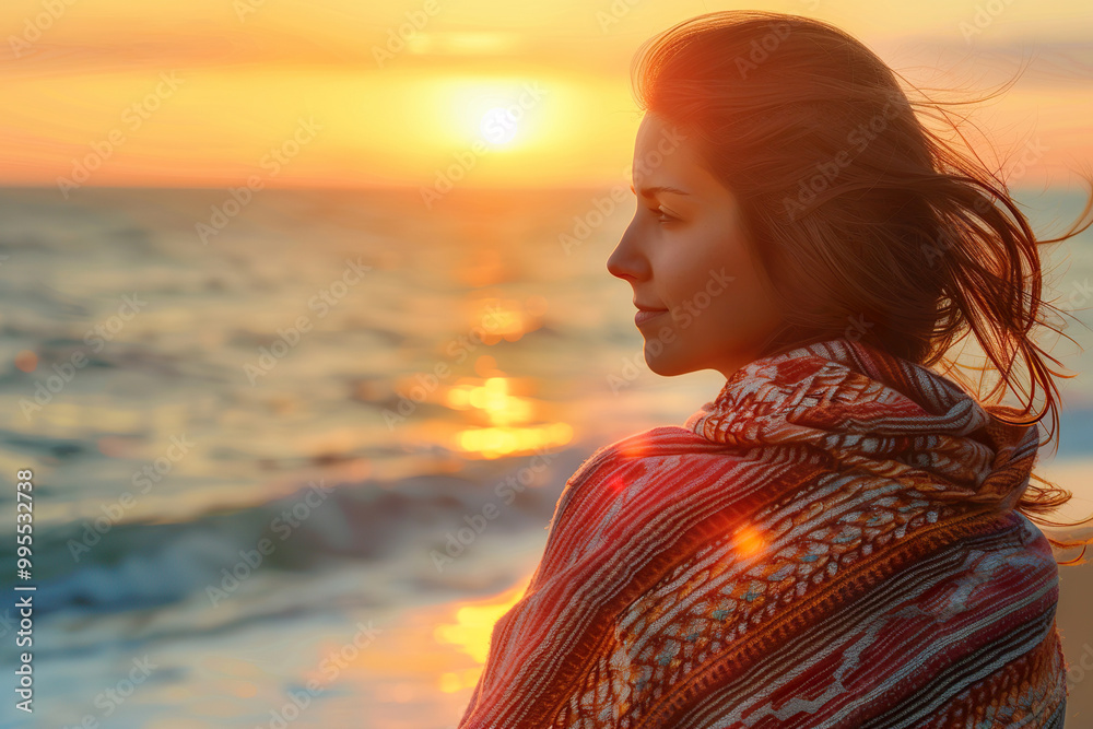 A woman is sitting on the beach, wrapped in a colorful scarf.,