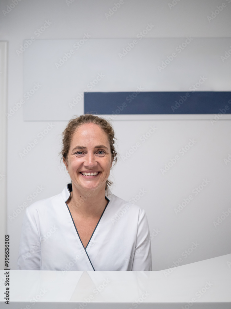 A cheerful receptionist with curly hair smiles warmly from behind a sleek front desk. The contemporary clinic features minimalist decor in light colors. A cheerful receptionist with curly hair smiles warmly from behind a sleek front desk. The contemporary clinic features minimalist decor in light colors.