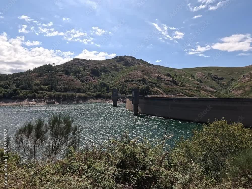 View of Peneda-Gerês dam and reservoir with hills and rippling water under a clear sky
View of Peneda-Gerês dam and reservoir with hills and rippling water under a clear sky