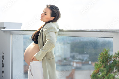 Stylish pregnant woman in a suit on the balcony. Pregnancy and style concept.