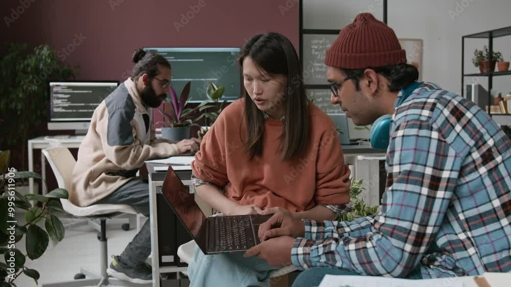 Medium shot of Asian female product manager and Indian male website designer sitting in office, studying software prototype on laptop screen and discussing improvements for better user experience Medium shot of Asian female product manager and Indian male website designer sitting in office, studying software prototype on laptop screen and discussing improvements for better user experience