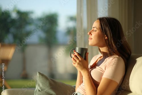 Woman smelling coffee sitting in a sofa at home at sunset